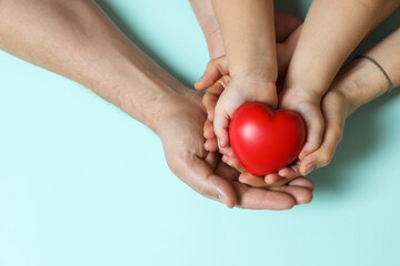 Parents and child holding red decorative heart on light blue background, top view. Space for text