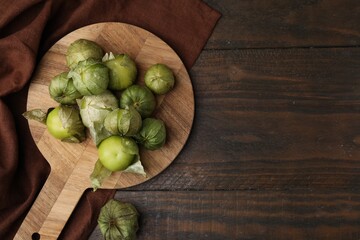 Fresh green tomatillos with husk on wooden table, top view. Space for text