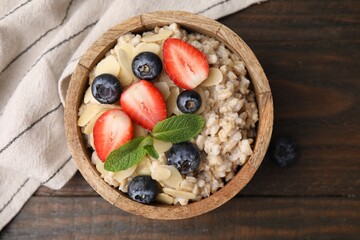 Tasty oatmeal with strawberries, blueberries and almond petals in bowl on wooden table, top view