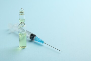 Glass ampoule with liquid and syringe on light blue background. Space for text