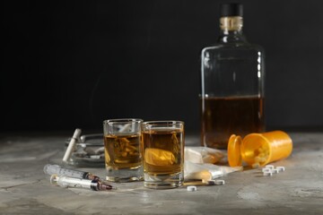 Alcohol and drug addiction. Whiskey in glasses, syringes, pills and cocaine on grey table - obrazy, fototapety, plakaty