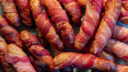 Sticky bacon-wrapped sausages spread on a plate to cool down, meat-based appetizer and popular...