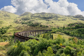 The Glenfinnan Viaduct curves through the rugged terrain, framed by undulating hills and a tapestry...