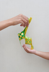 The hand of a mother giving a small traditional ketupat made from yellow and green ribbon to her kid
