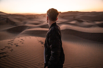 Young man gazing over the sandy desert at sunset