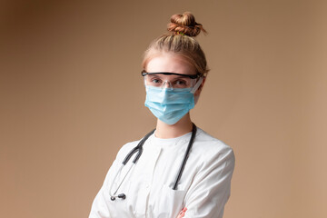 Professional Female GP Doctor Posing in Doctor's Smock and Facial Mask and Endoscope With Hands Folded Over Beige.