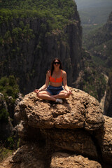 Naklejka na ściany i meble Girl meditates in green canyon amidst verdant rocky mountains. Perfect for adventure tours, expeditions, and mountain excursions organized by travel agencies. Promotes mountain and ski resorts.