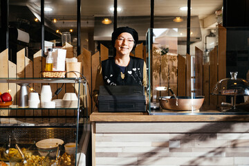 Smiling Woman Worker Poses Behind Counter in a Take Away Food Shop Looking at Camera - obrazy, fototapety, plakaty