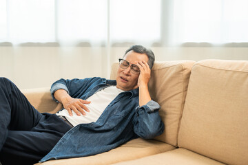 Asian mature old man sitting headache tired on sofa at home. Portrait of serious depression sadness...