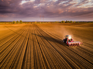 Aerial shot of a farmer seeding, sowing crops at field. Sowing is the process of planting seeds in the ground as part of the early spring time agricultural activities. - obrazy, fototapety, plakaty