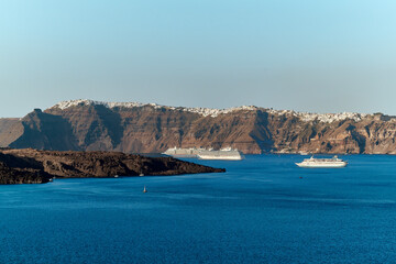 View with cruise ships of the volcanic caldera of Nea Kameni and the village of Imerovigli in the background, from the southwestern part of the island of Santorini - obrazy, fototapety, plakaty