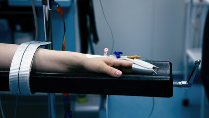 Close-up of a pulse oximeter on a patient's finger during surgery. The patient lies on a hospital...