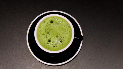 Closeup of a cup of matcha green tea drink, with some froth on the top. With a black cup and a black background.