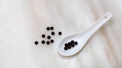 White soup spoon, with traditional Chinese medicine in form of small black balls. On marble surface.