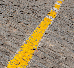 Texture of dark grey cobblestones with yellow stripe as road marking