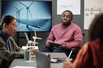 Young confident businessman in wheelchair sitting by interactive board and making presentation of windmill energy project to colleagues - Powered by Adobe