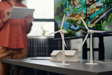 Two windmill models standing on grey desk next to plastic house mockup and interactive board with visual template of new business project