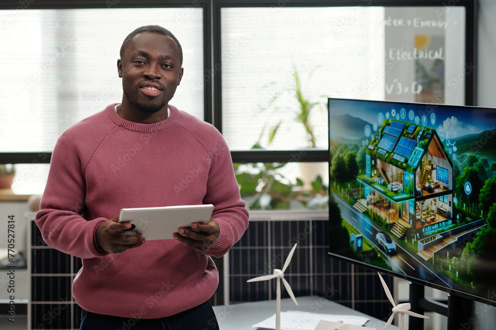 Poster young smiling businessman with tablet networking or organizing work and looking at camera while prep