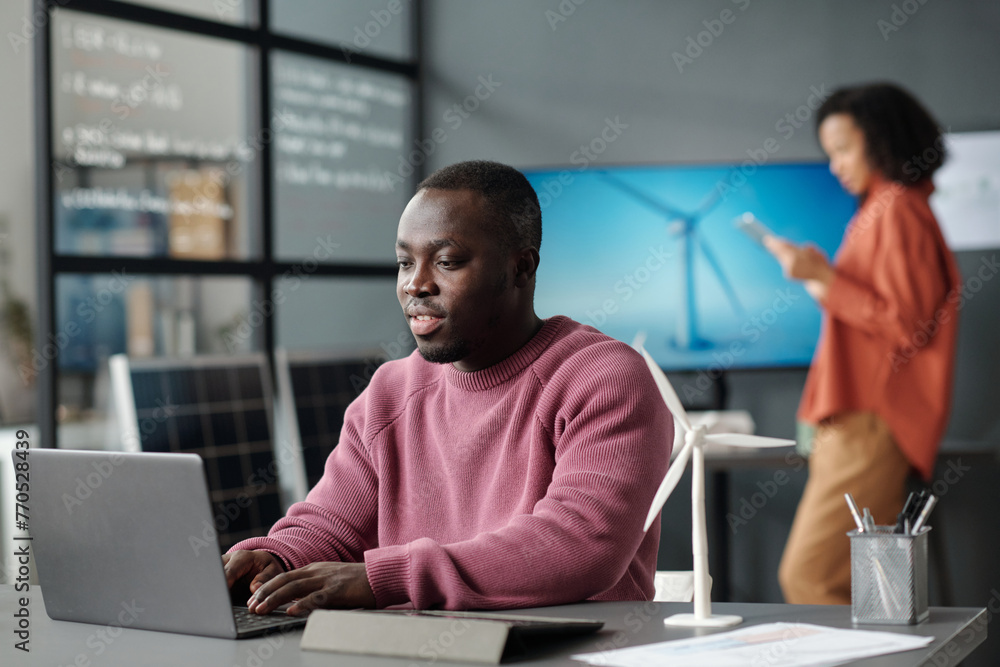 Poster young confident businessman typing on laptop keyboard and looking through information on screen whil