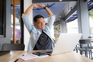 Asian man Tired and exhausted with blue shirt using laptop and mobile phone in coffee shop, online...