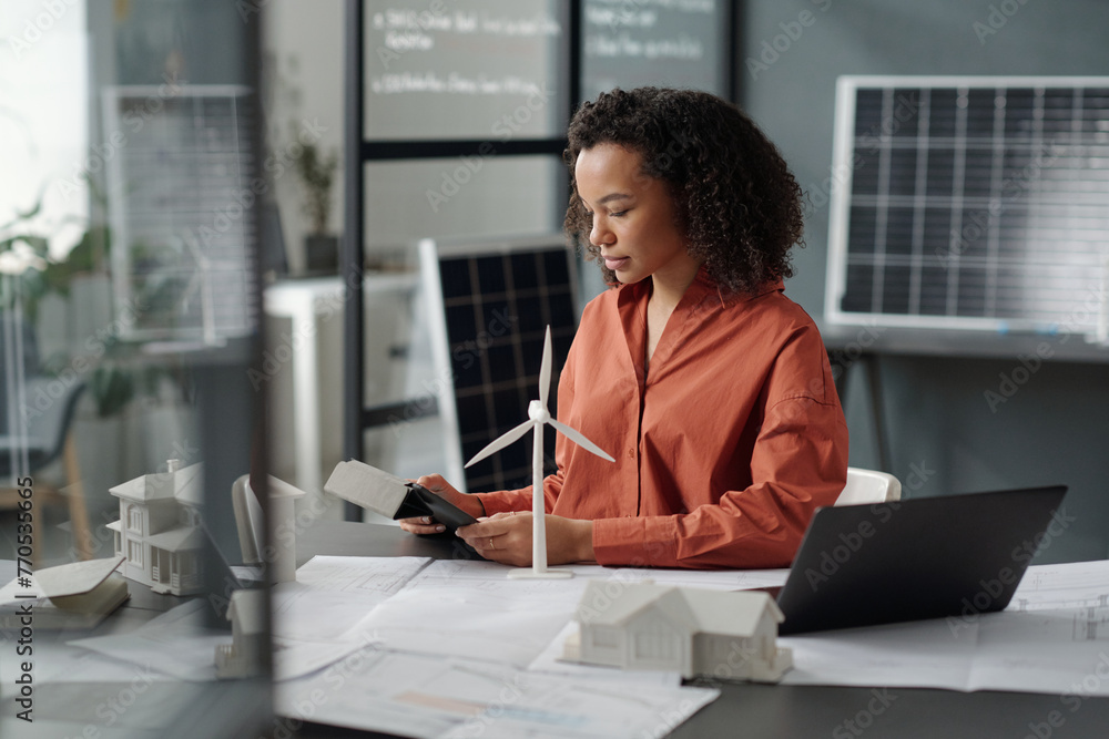 Poster young serious businesswoman looking at tablet screen and analyzing online data while sitting by desk