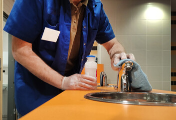 A Caucasian man washes and disinfects the faucet and sink in a public toilet, cleaning services.