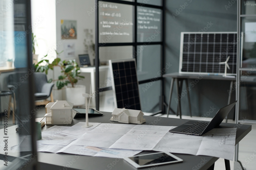 Poster blueprint with sketches surrounded by digital tablets, laptop and models of houses and windmill on w