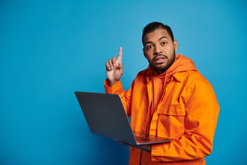 confused african american man in orange outfit with laptop came up with idea on blue background