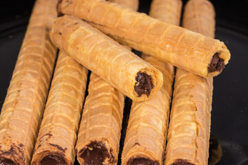 Wafer tubes with chocolate cream on black dish close-up
