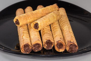 Wafer tubes with chocolate cream on black dish close-up