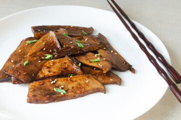 Eryngii mushroom fried with sesame and green onion on a white plate. The process of cooking...
