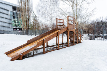 A wooden slide stands on a snowcovered slope in the park