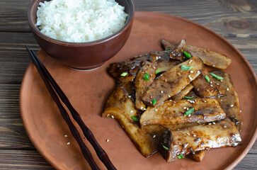 Eryngii mushroom fried with sesame and green onion on a ceramic plate and white boiled rice in a...