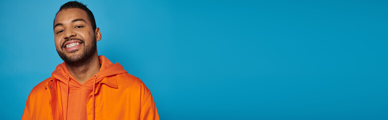 banner of happy african american man in his 20s smiling broadly with leaning head on blue background