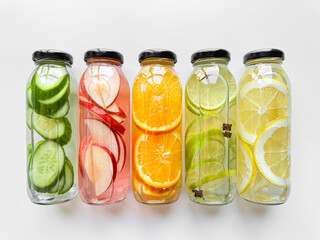 Fruit and vegetable detox drinks in glass bottles on white background. Horizontal line up with copy space. Natural infused water variety concept for healthy lifestyle.