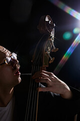 Male musician playing double bass against black background with lights elements. Classical music...