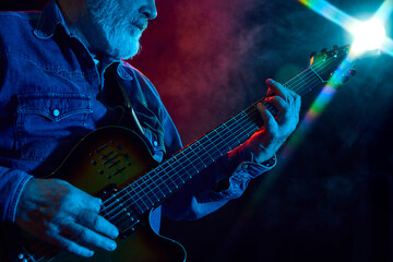 Senior bearded man playing guitar against dark background with dusk element. Concept, performance....
