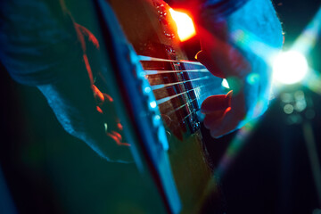 Intense close-up of bass guitar playing, with colorful stage lights. Male musician, solo performer playing on live concert. Concept of music, instruments, concert, sound, equipment, festival