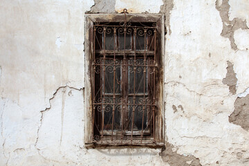 Fototapeta na wymiar Window with rusty wrought iron window railing of an abandoned house. Peeling paint and cracks on the facade of the house.