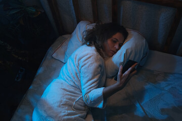Insomnia. Woman using smartphone lying awake in bed at night
