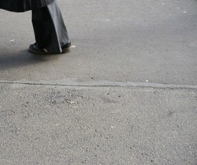 Frauenbein mit breiter grauer Schlaghose aus Stoff steht auf grauem Gehweg in Stadt bei Sonne am...