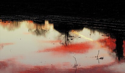 Grosse Wasserpfütze in Acker mit Reflektoren des Abendhimmels bei Sonnenuntergang