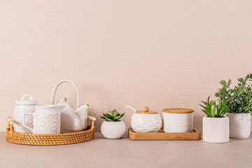 White ceramic tea set on round wicker tray among indoor plants on kitchen countertop. Kitchen...