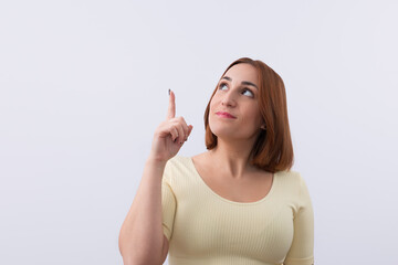 Studio portrait of pretty woman looking and pointing her finger up isolated on white background. Copy space. Promotion and marketing concept - obrazy, fototapety, plakaty