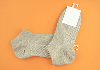 New textured gray cotton socks with an empty white label (tag) on an orange background closeup