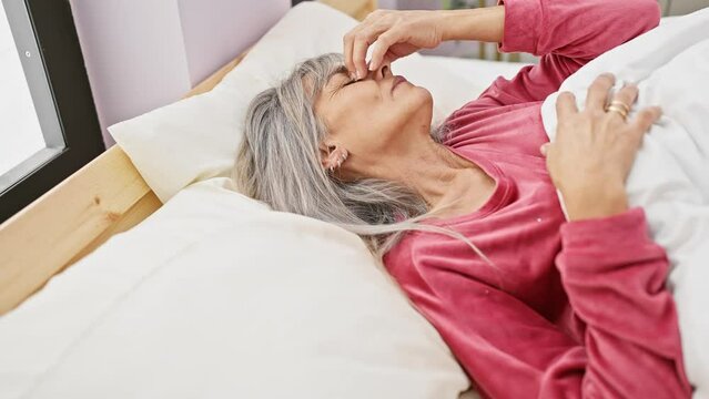 Mature, hispanic woman with grey hair experiencing discomfort in bed at home, depicting healthcare or wellness.