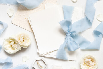 Cards tied with a light blue ribbons near cream roses on white table top view, wedding mockup