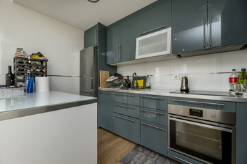 Open kitchen of a loft apartment with gray-green furniture with a white island with a smooth surface