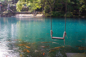 A traditional swing located right above the blue lake and surrounded by shady green trees and...