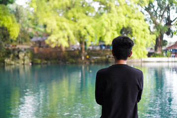 Fototapeta premium A man poses looking at the blue lake and the trees in front of him